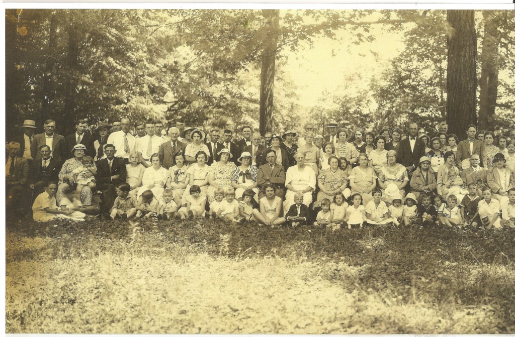 Left side of the Schaber's Grove Community Picture. Pictured are approximately over 100 people on the grass in front of some trees.